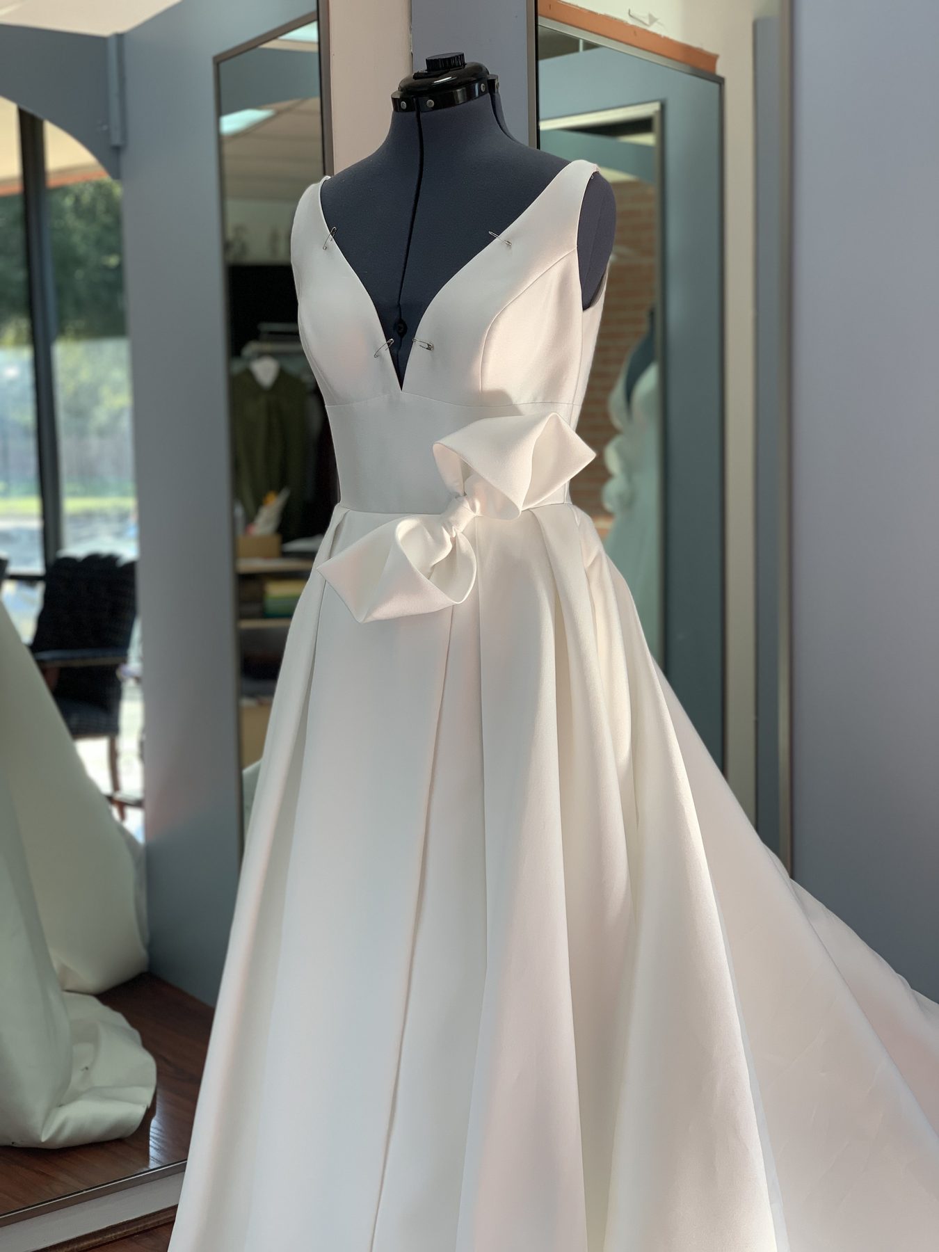 Wedding gown mid-alteration, pinned with a sculpted bow at the waist